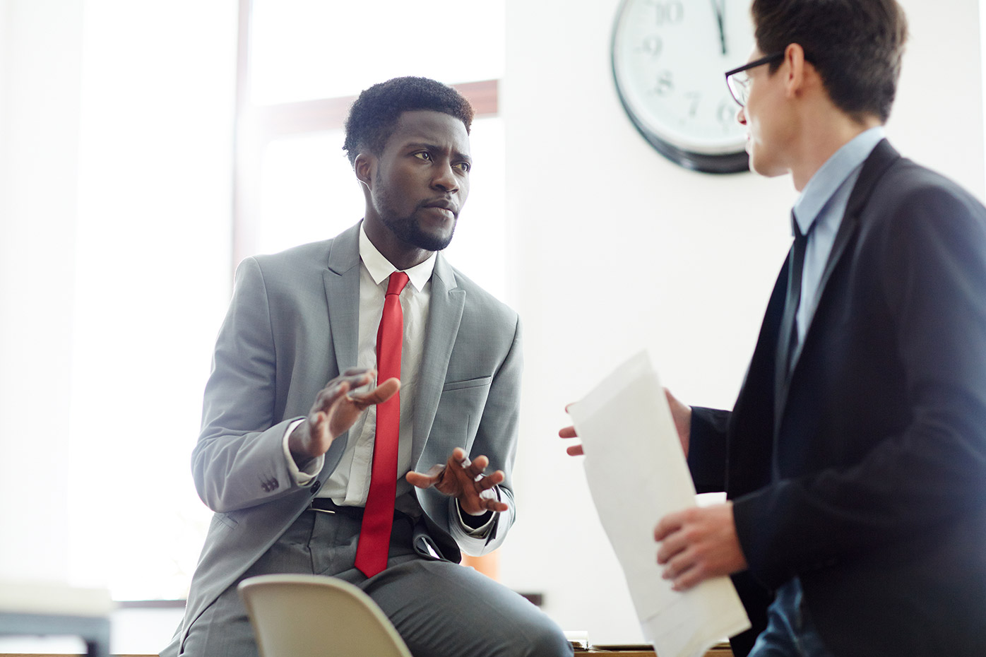 Man in gray suit with red tie having a business discussion with another man