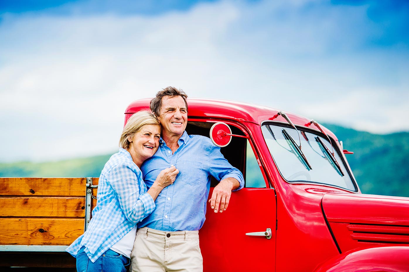 Senior couple standing next to a red pickup truck