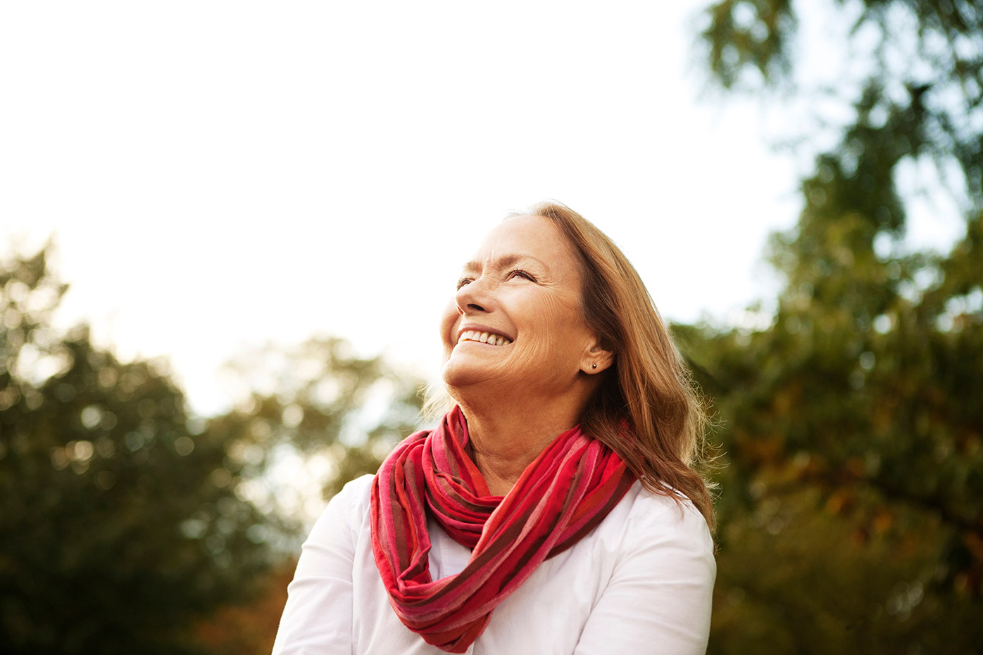 Senior woman with a red scarf standing in a wooded field