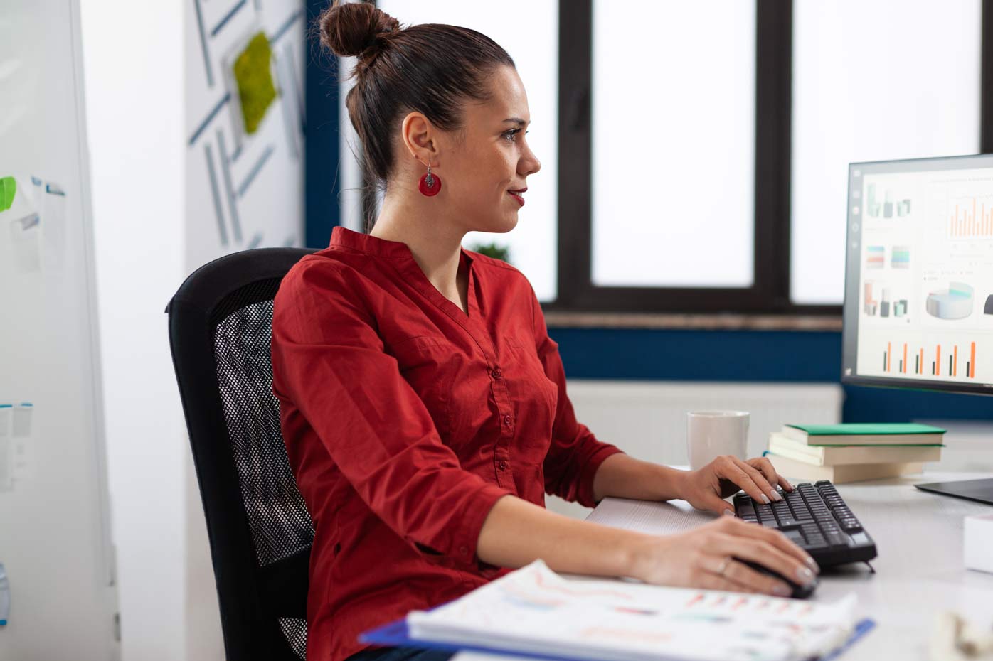 A woman in a red shirt works on charts and tables at her computer