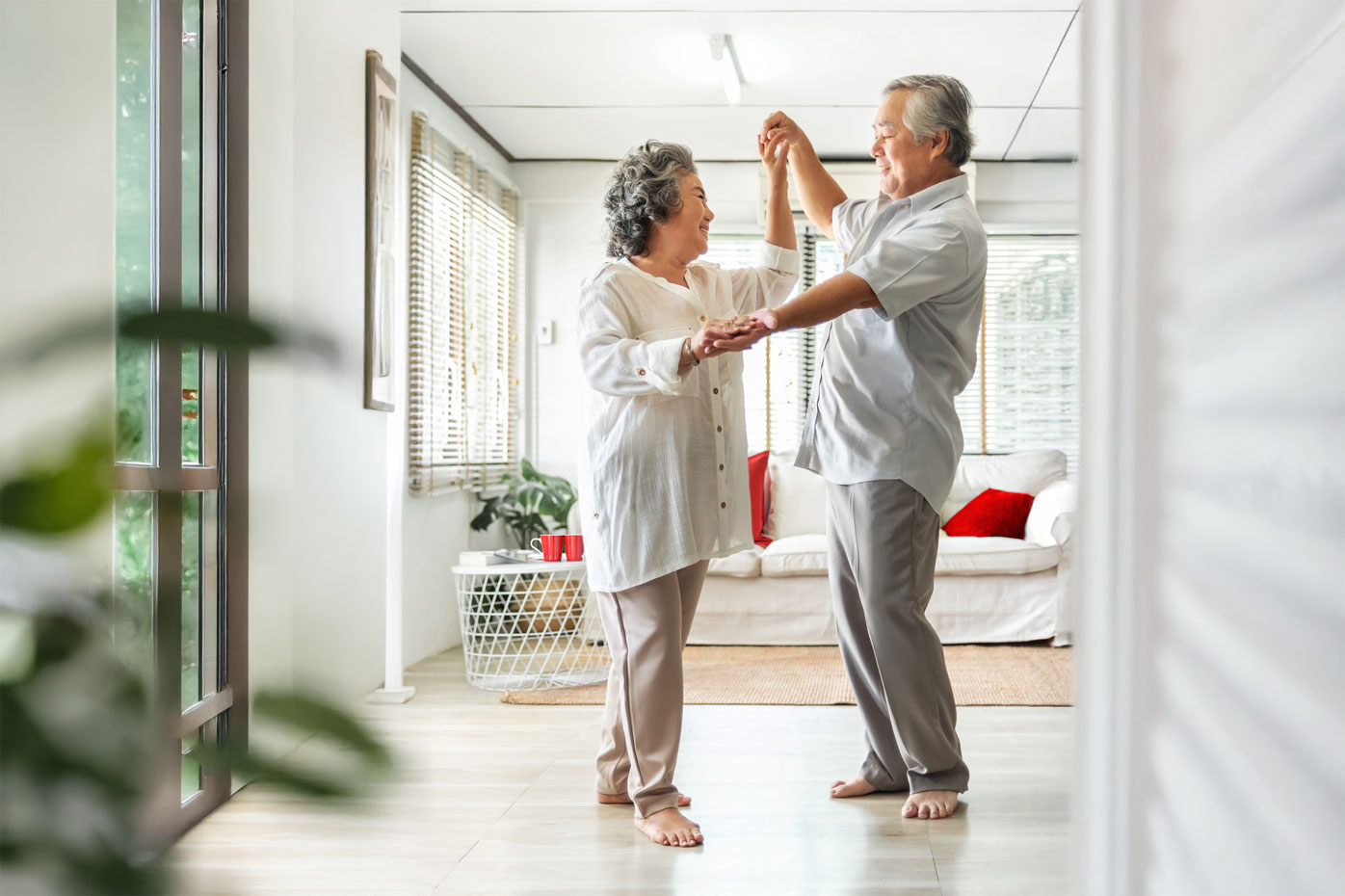 An older Asian couple dances barefoot in their living room