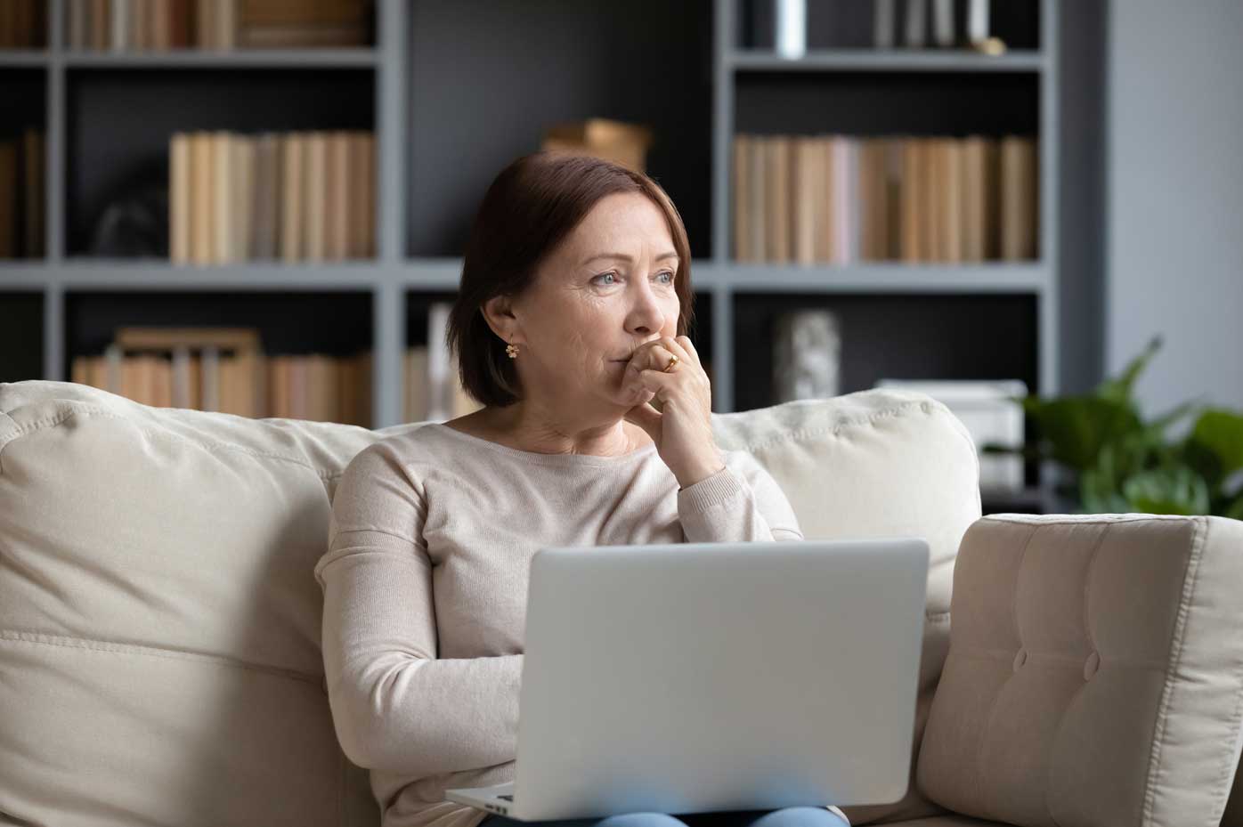 A woman seated by a computer looks pensively into the distance