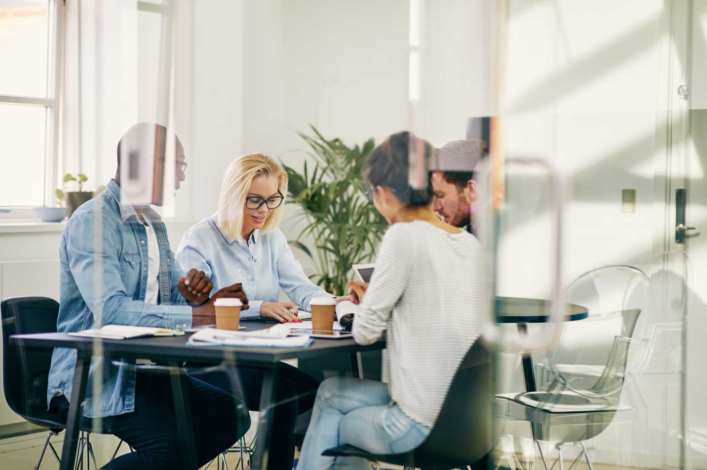 A cluster of workers meet in a glass walled office