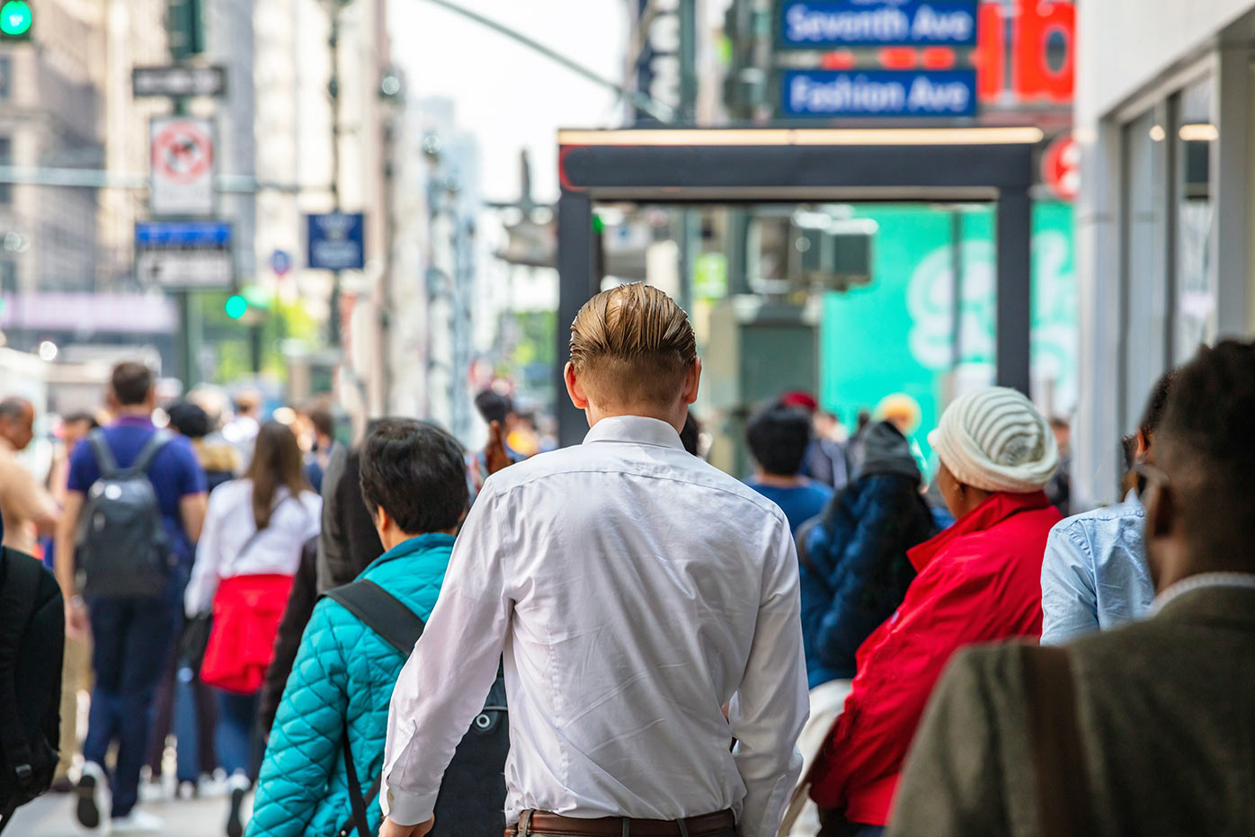 Busy city street with people walking away and a man in white shirt in the foreground