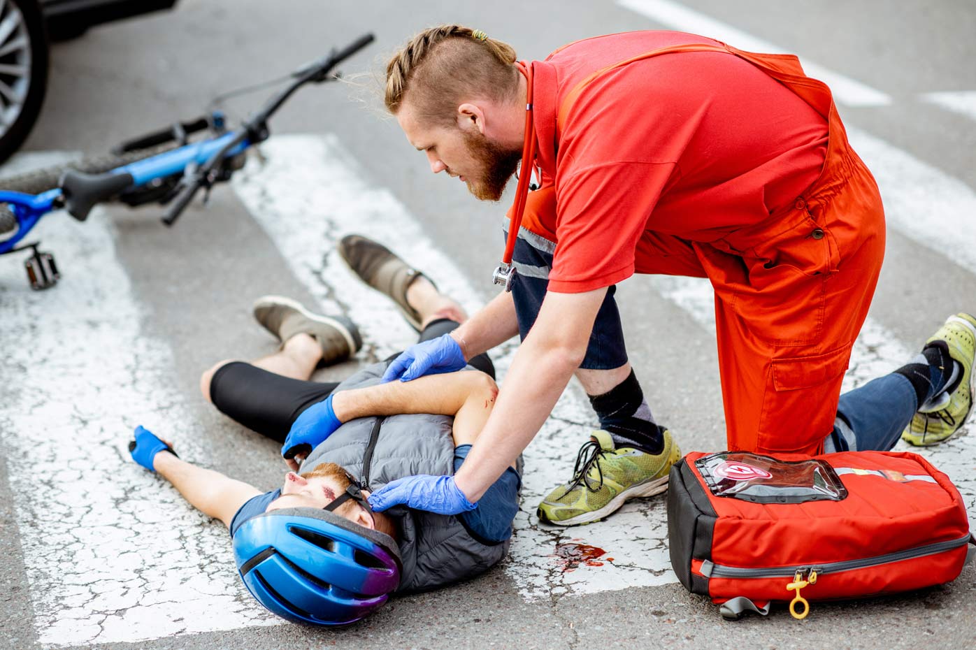 A paramedic dressed in red assists a cyclist who was injured and is lying in the road.