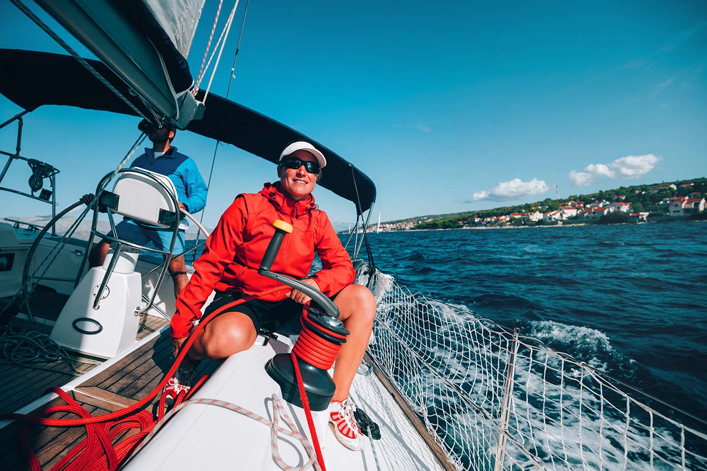 Man in red jacket operating a crank on a sailboat