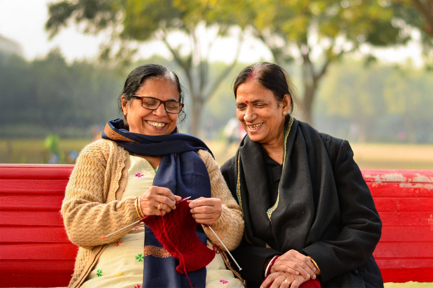 Two elderly Indian women sitting on a red bench