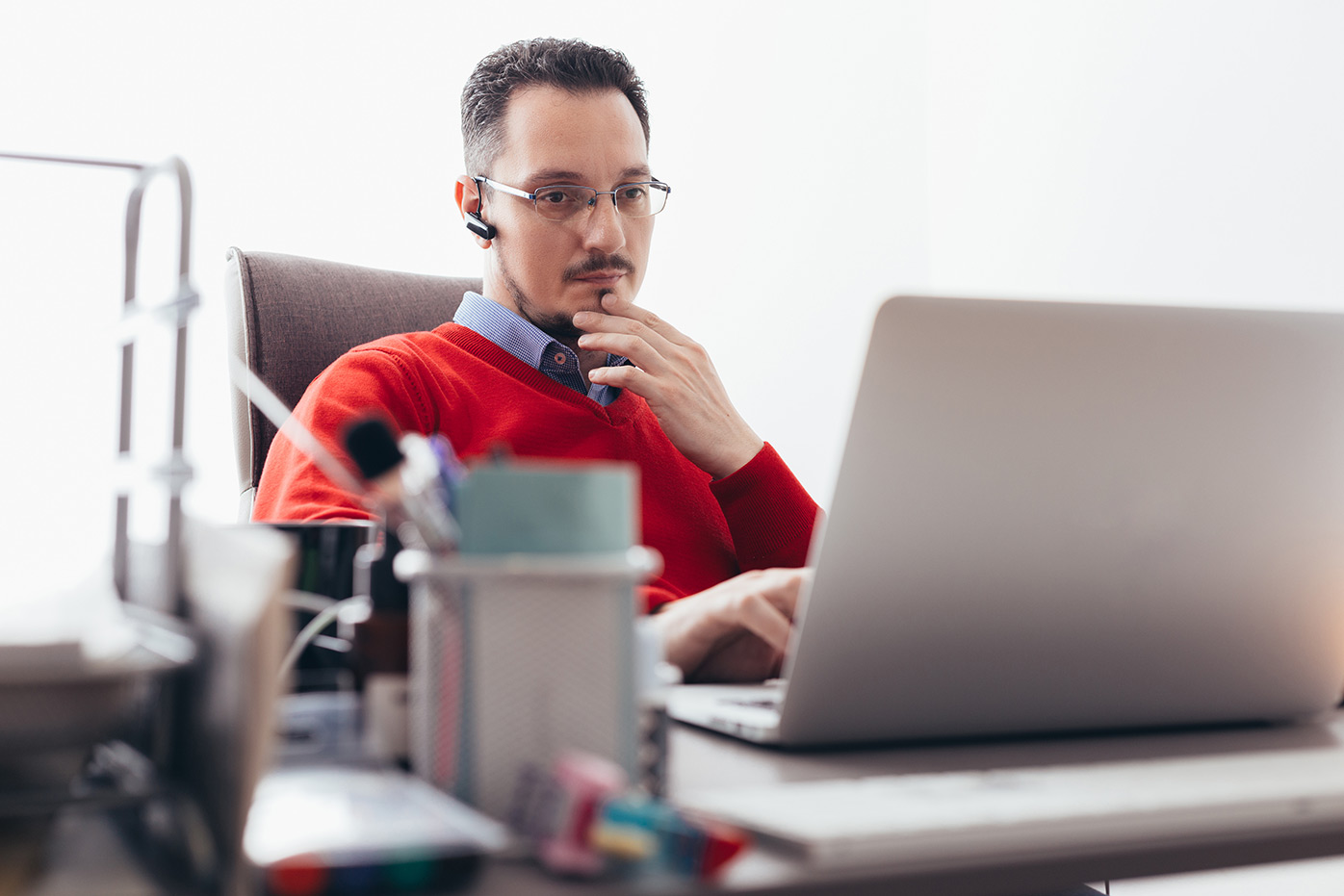 A man wearing a red sweater looking at his laptop