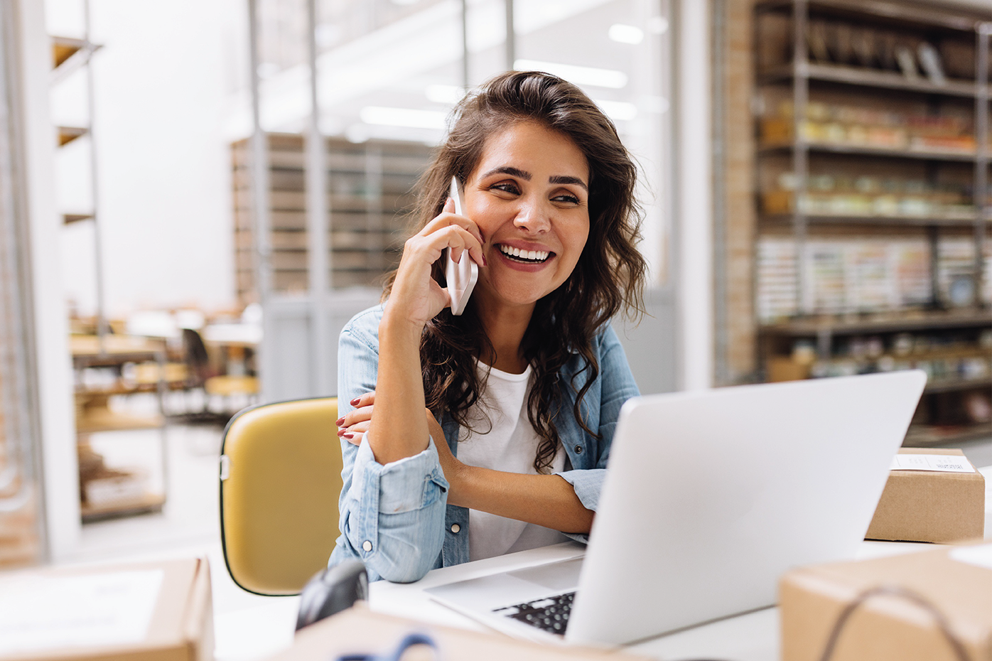 A smiling businesswoman talks on a smartphone while seated before her laptop