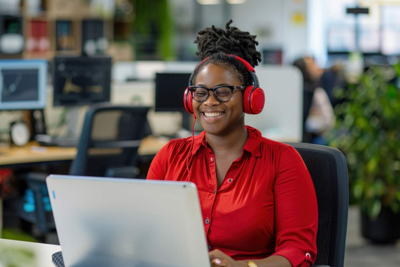 A female employee wears red headphones and smiles at her computer