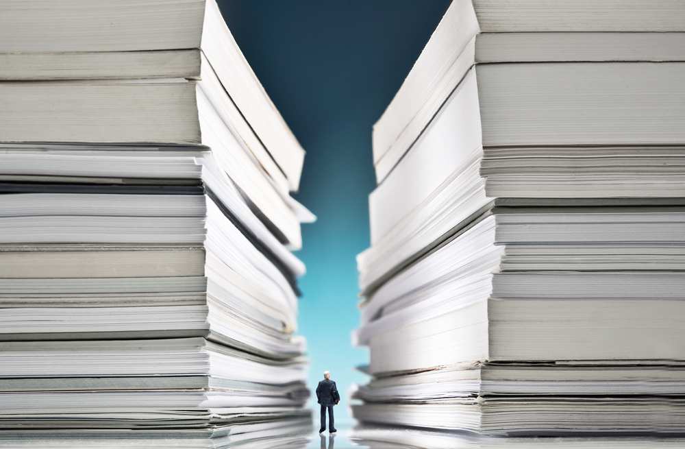 Overwhelming Paperwork towering over small figure