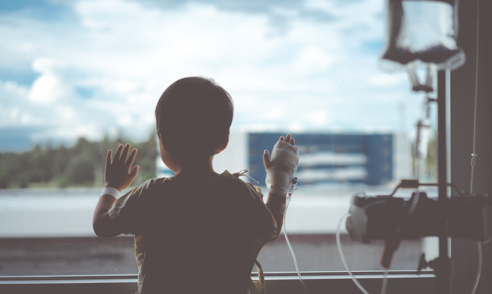 Child undergoing chemotherapy gazes out the window of a hospital