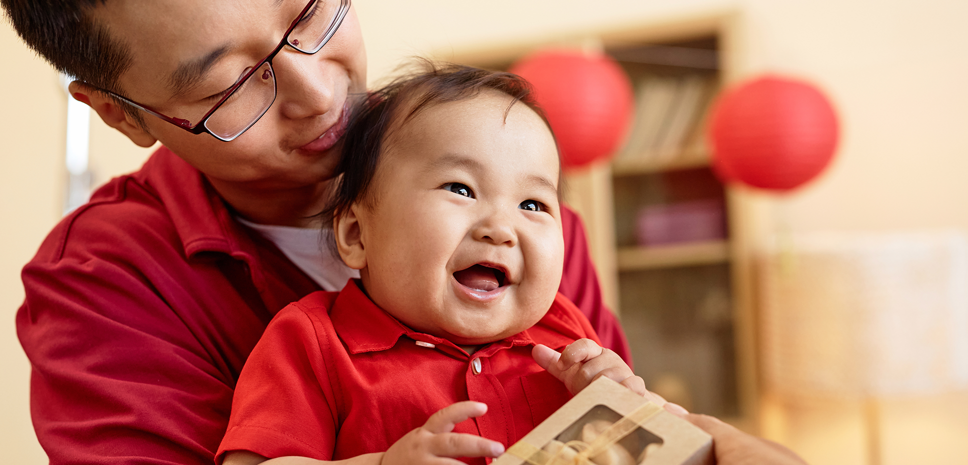 A giggling Asian baby leans against his father