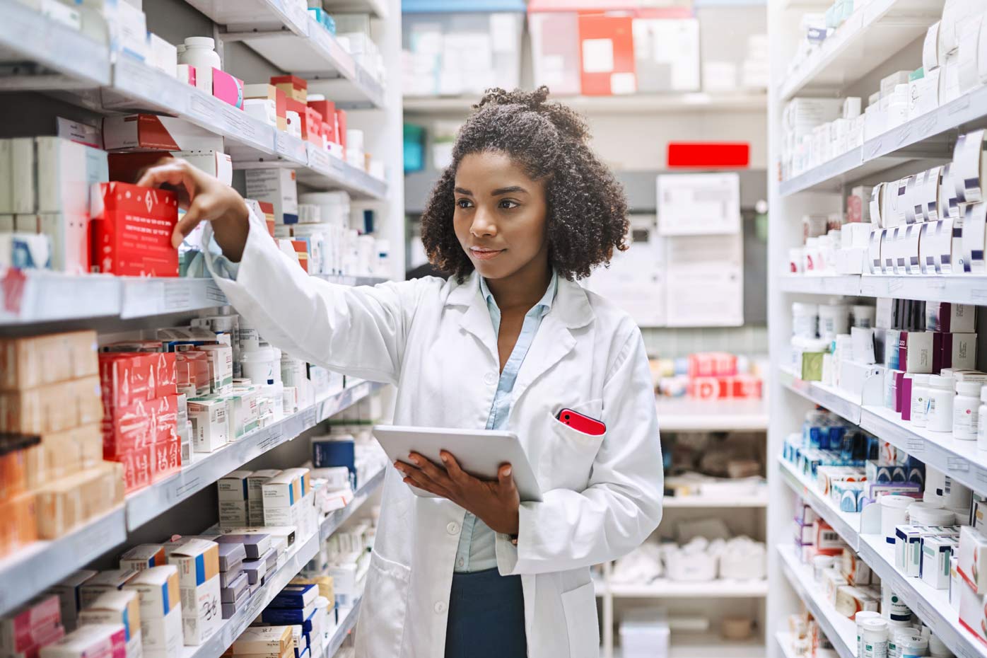 A pharmacist reaches for medication while walking down the aisle of a pharmacy