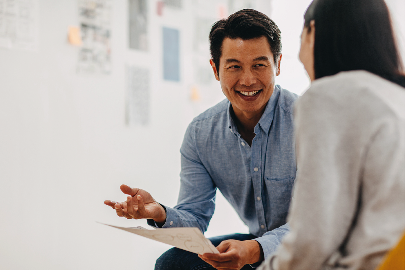 A man smiles while explaining a document to a colleague