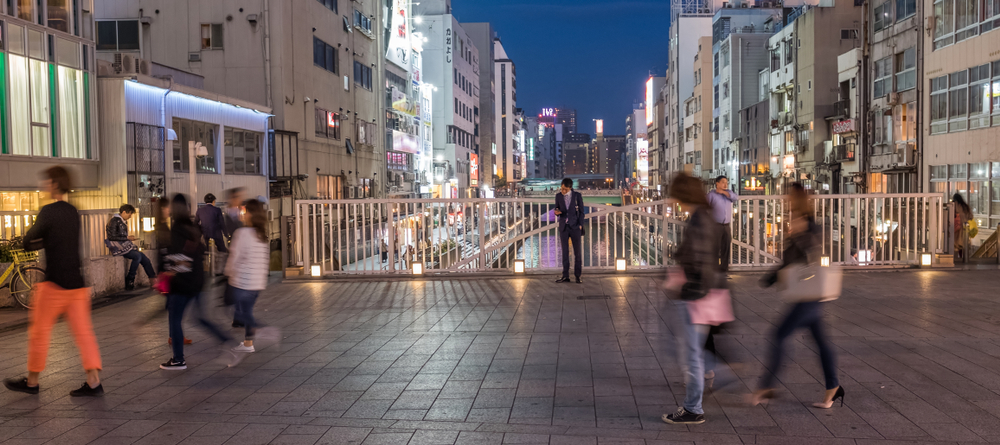 A busy street scene with an individual paused amid a passing crowd